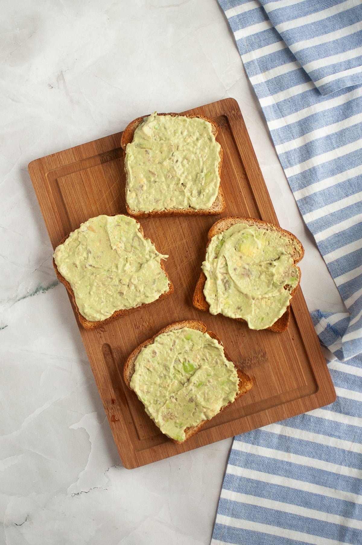 Avocado mayo is spread onto toasted bread. 