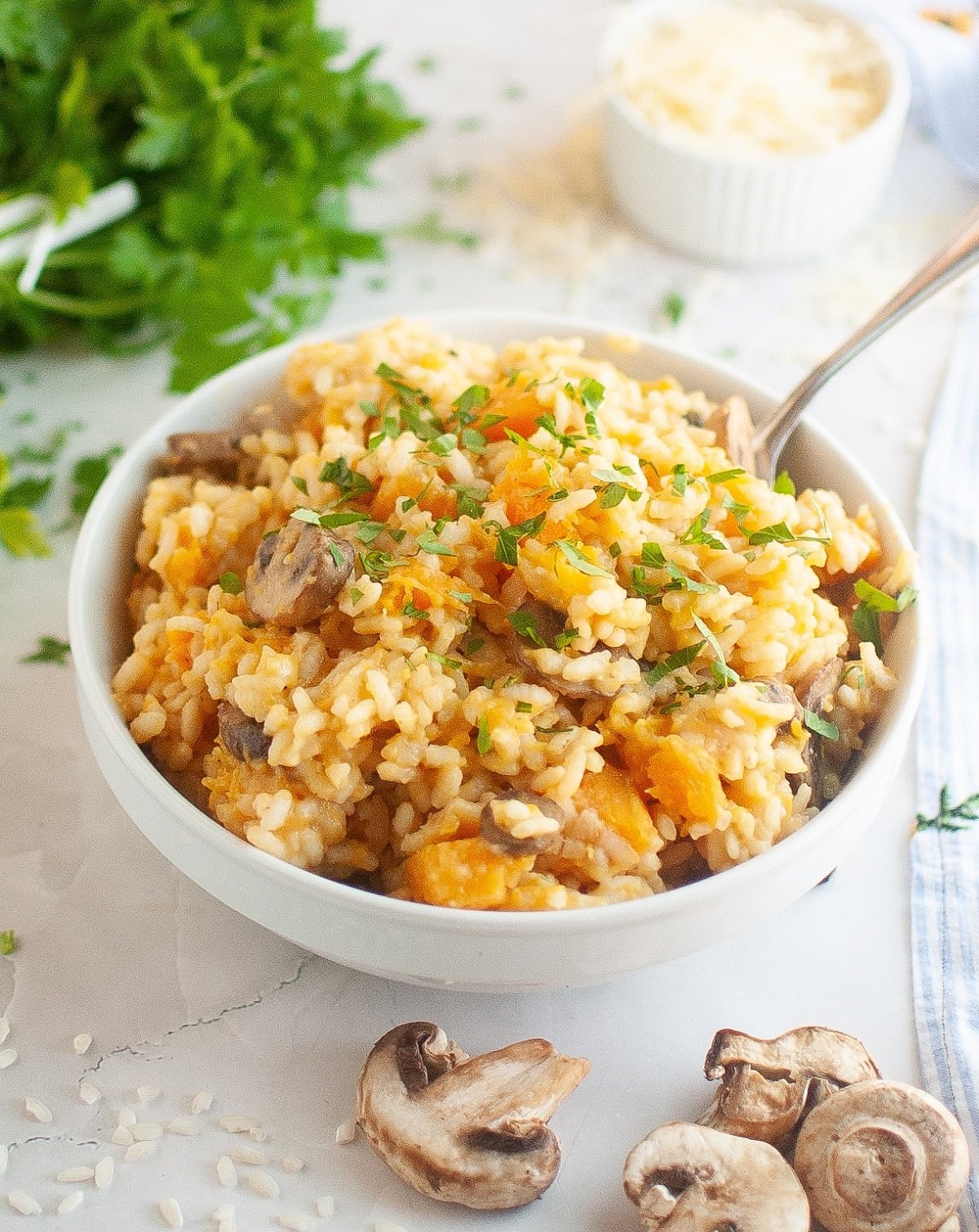 A spoon rests in a bowl of creamy risotto topped with mushroom and butternut squash.