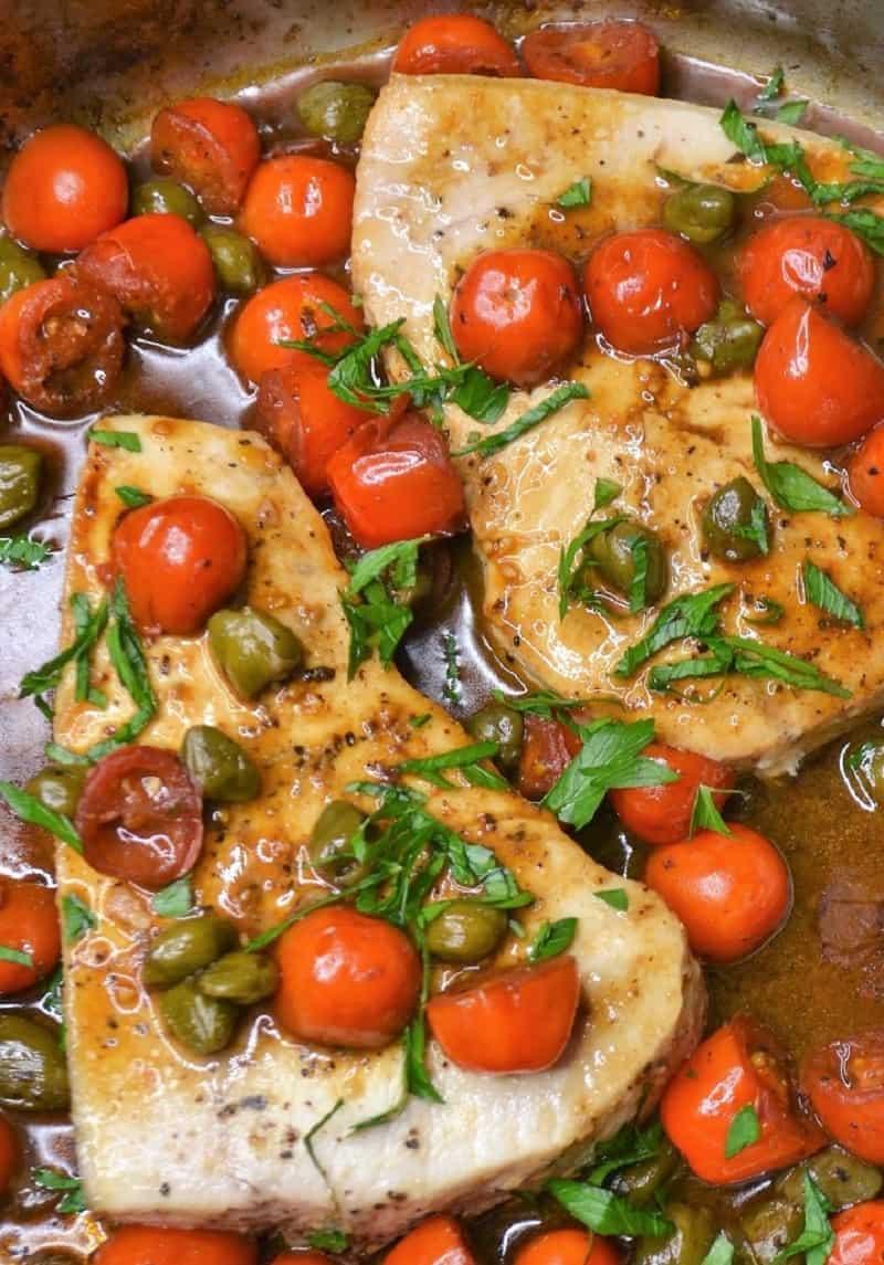 fish recipe Pan roasted swordfish topped with tomatoes and capers in a pan.