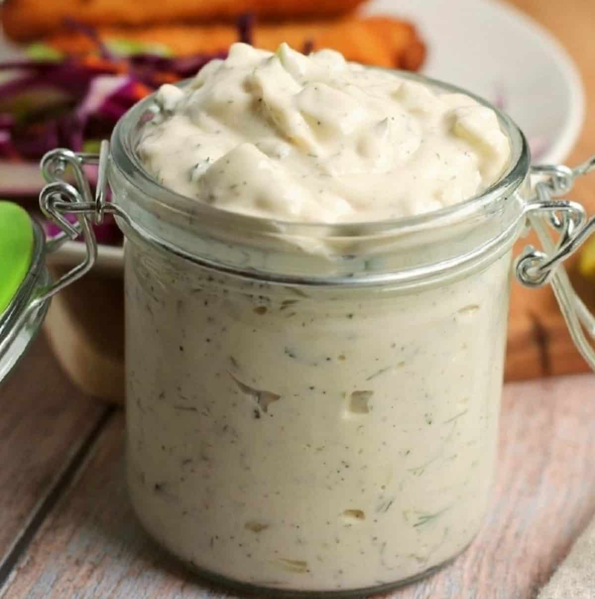 A glass jar is filled to the brim with creamy homemade tartar sauce.