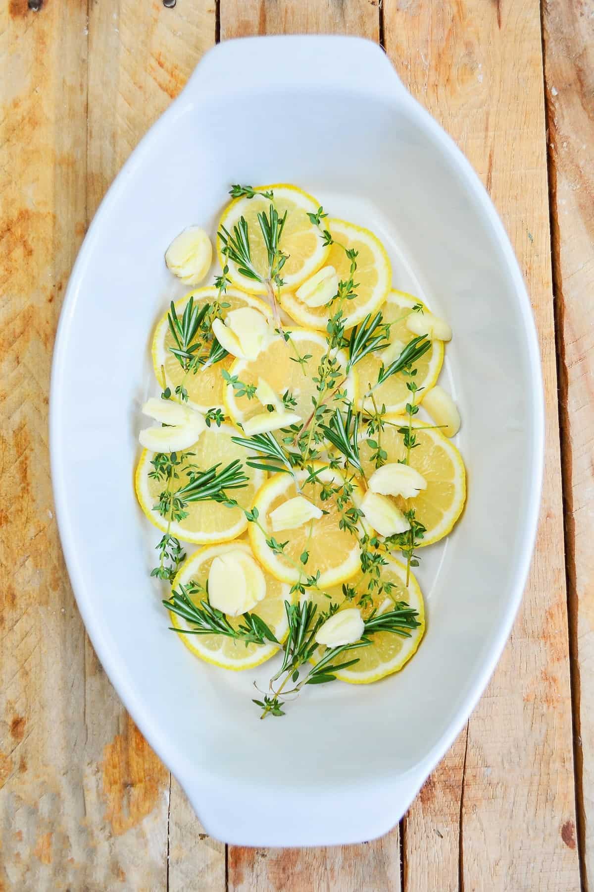 A baking dish lines with herbs and lemon slices. 