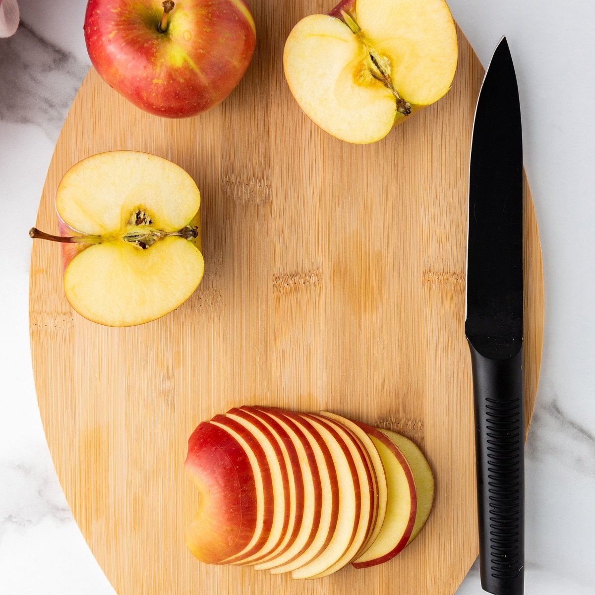 A cutting board with a knife and thinly slices apples. 