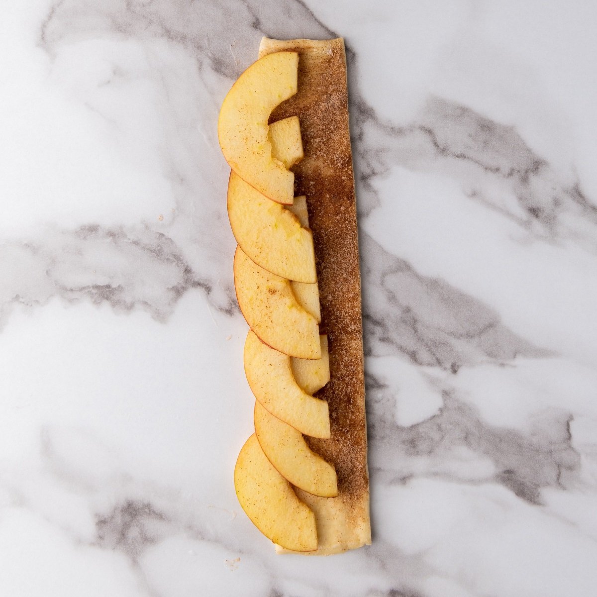 Apple slices are laid on a strip of puff pastry. 