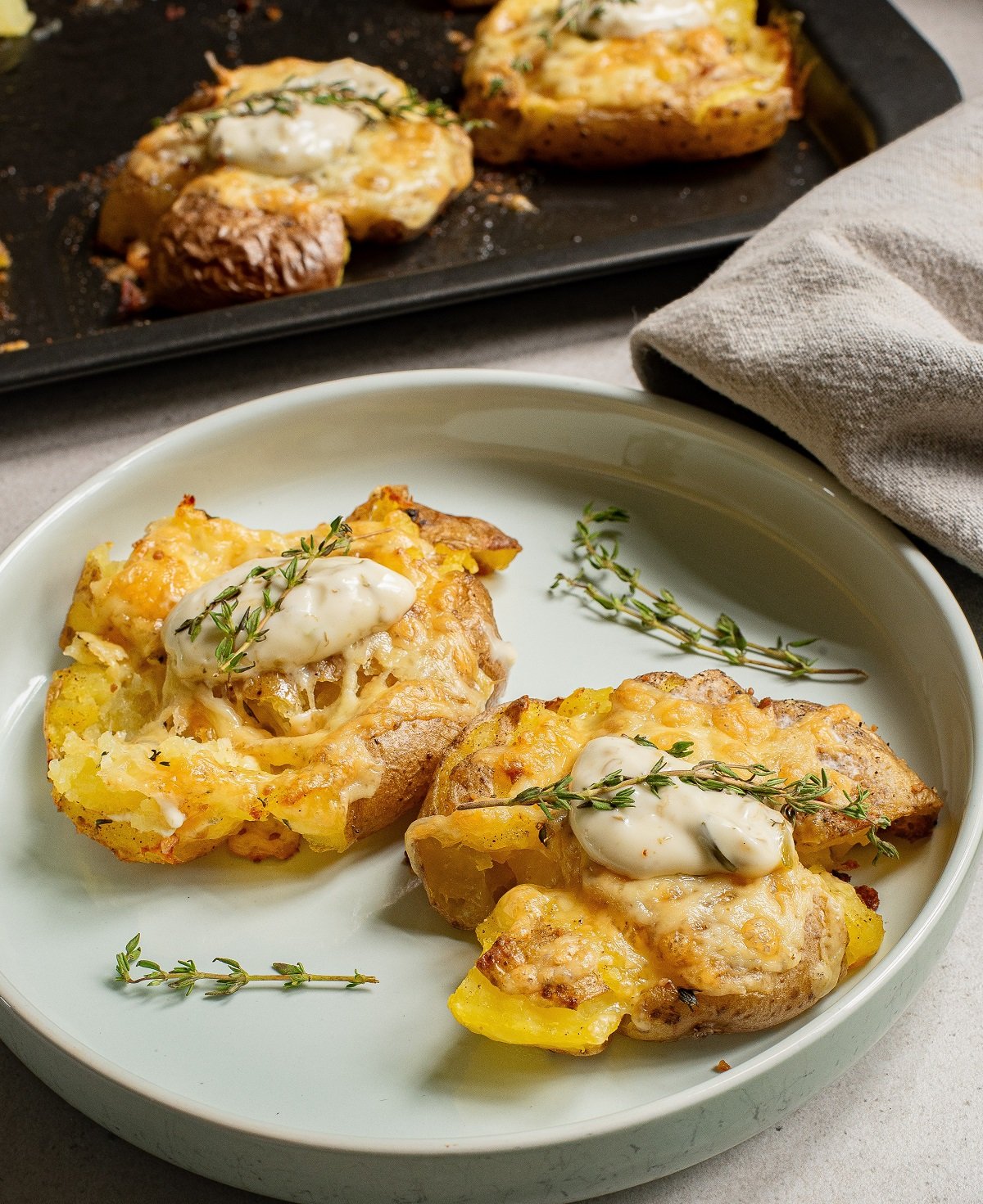 Crispy potatoes garnished with sour cream and herbs sit on a plate.