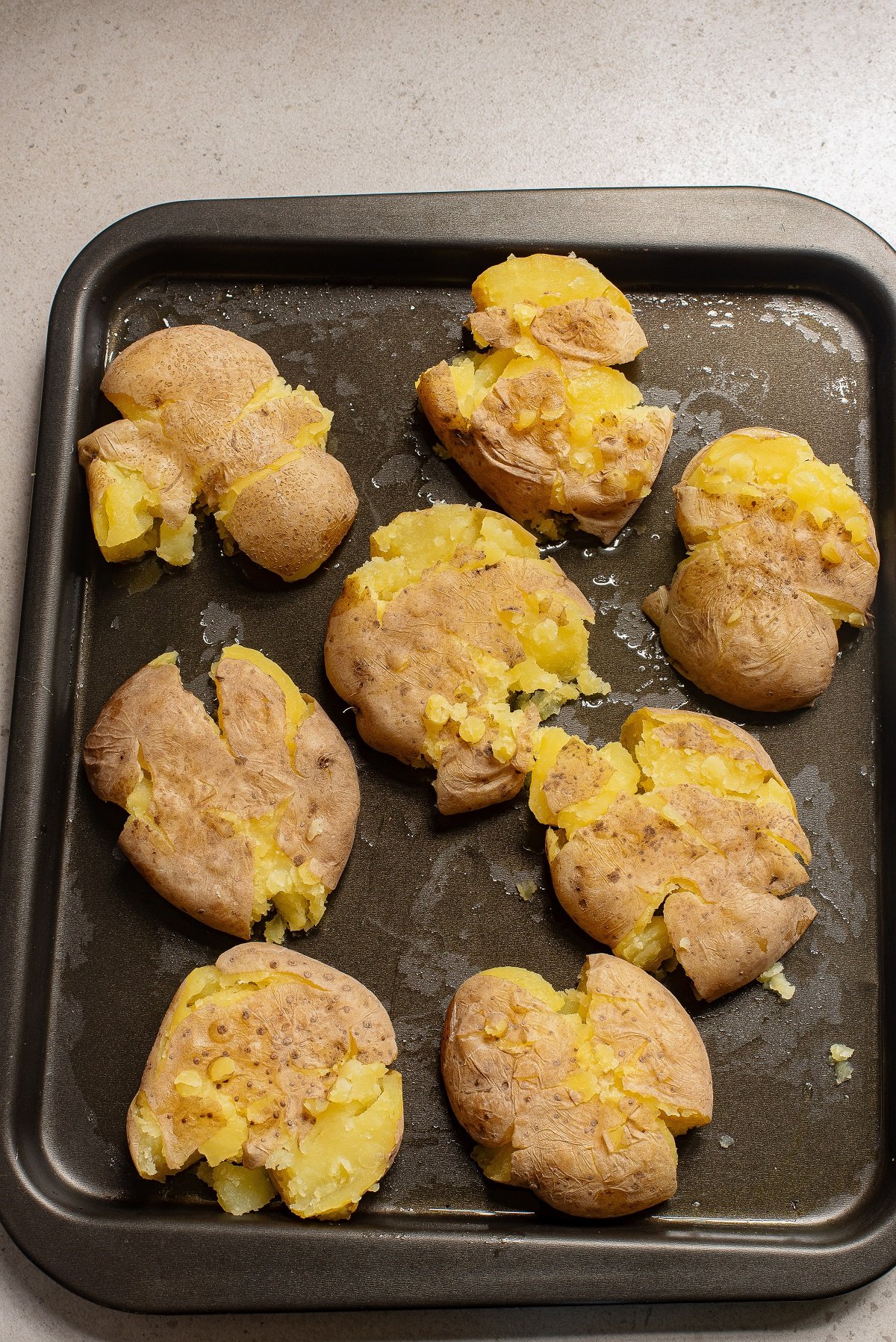 Smashed potatoes are arranged on a baking sheet. 