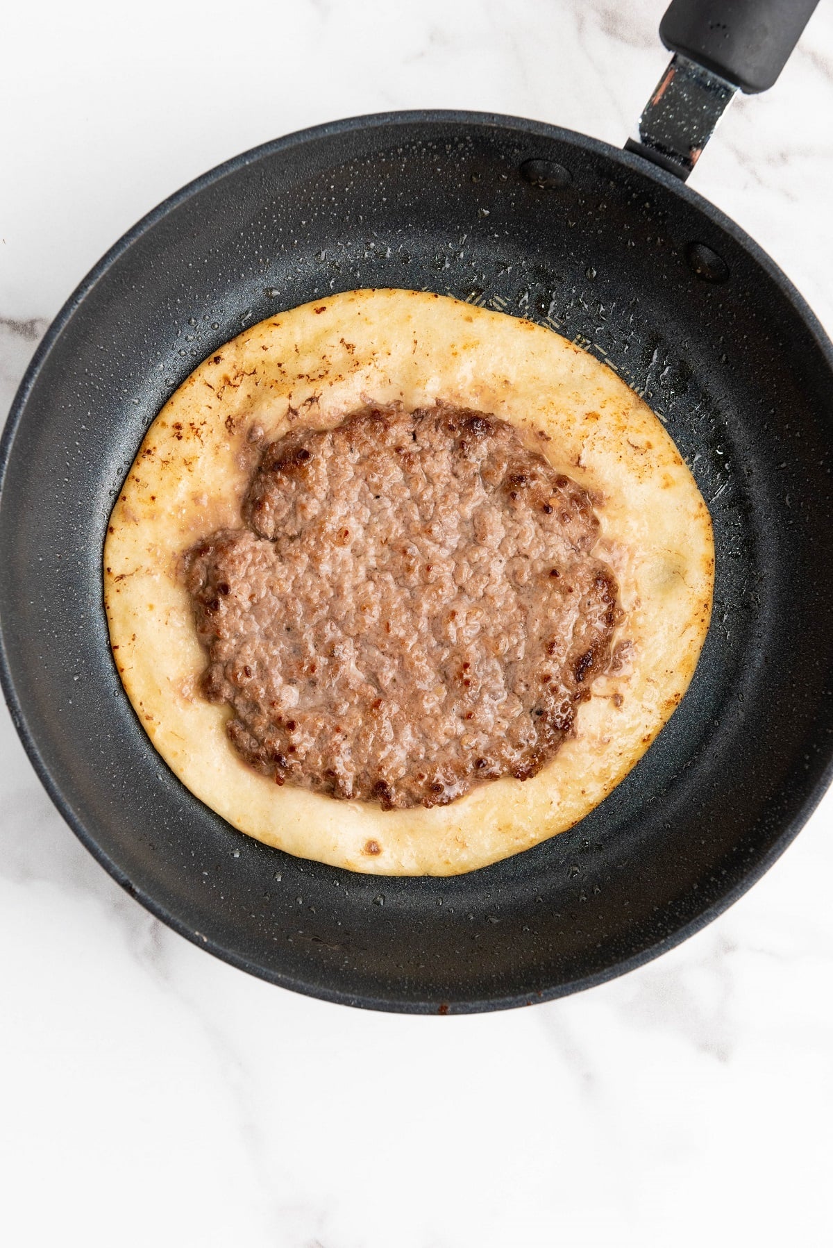 The burger patty and tortilla are cooked in a skillet.