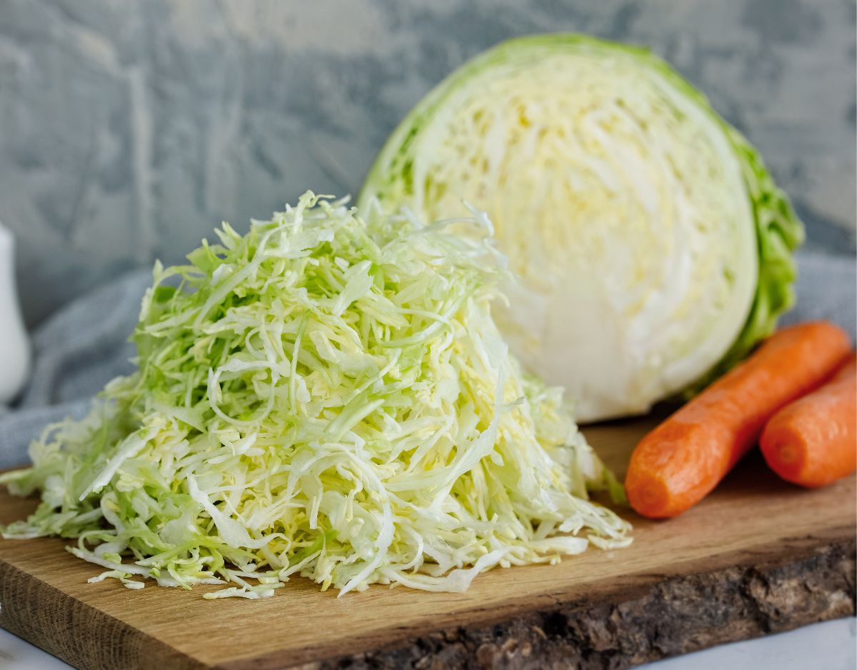 Freshly shredded cabbage on a cutting board with carrots and a head of cabbage. 