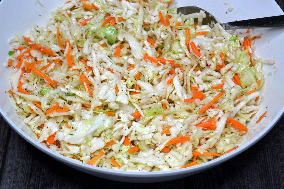 Coleslaw dressing is mixed with shredded cabbage and carrots. 