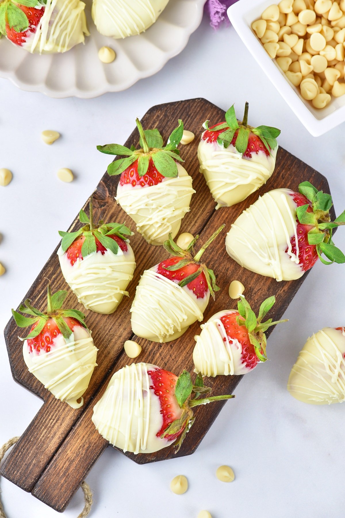 A wooden board topped with white chocolate covered cherries.