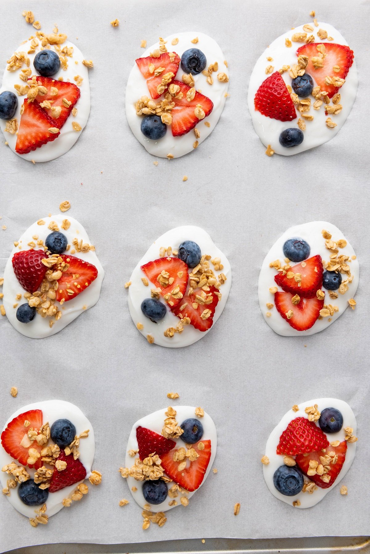 Dollops of yogurt topped with fruit on a baking sheet. 