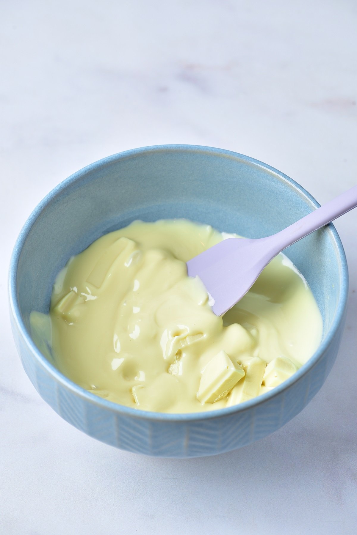 Melted white chocolate is stirred with a spatula. 
