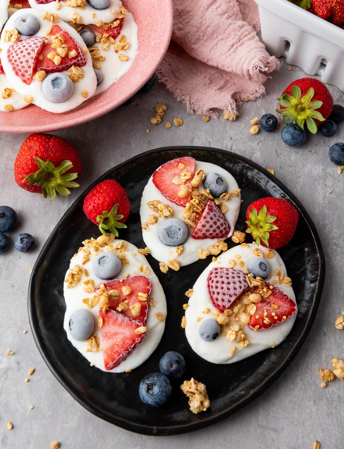Frozen yogurt bites with blueberries, strawberries and granola on a small plate. 