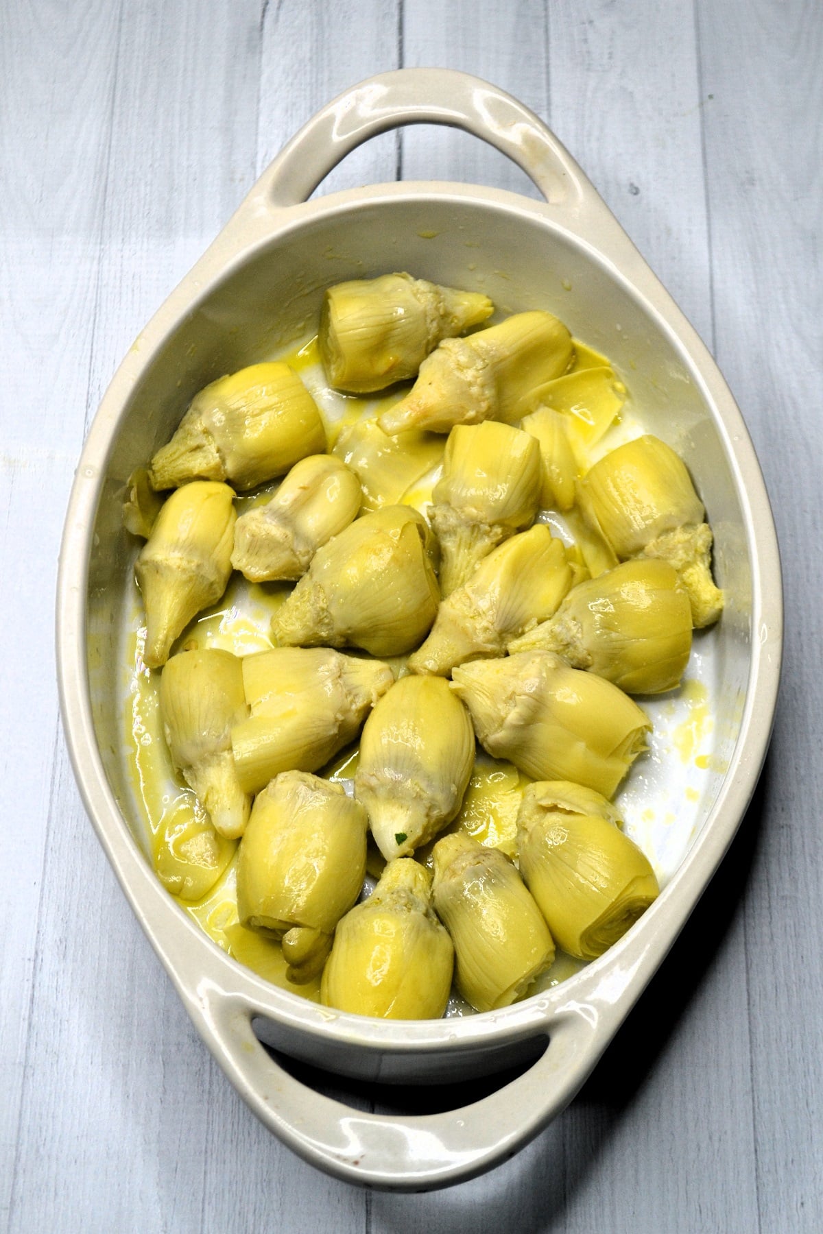 Artichokes are added to a baking dish and drizzled with olive oil. 