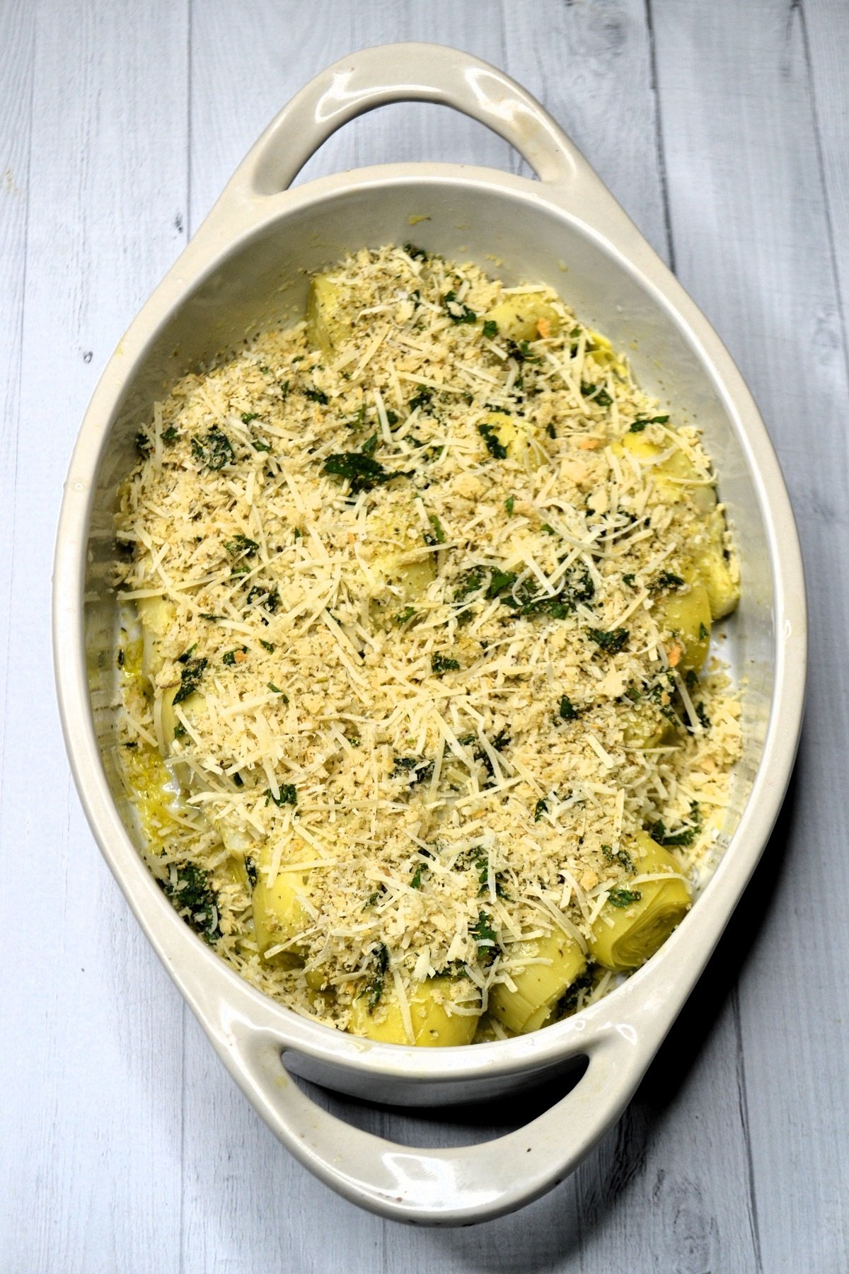 Breadcrumbs are sprinkled over artichokes in a baking dish. 