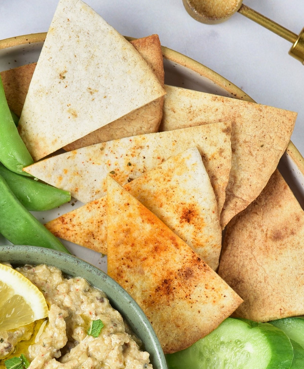 Air fryer pita chips on a plate beside hummus and fresh vegetables.