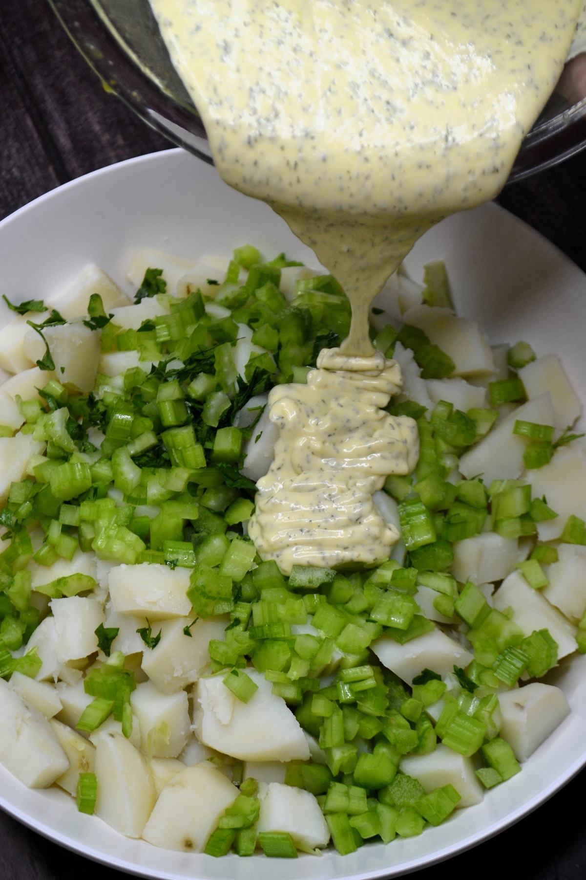 Dressing is poured over potato salad ingredients.