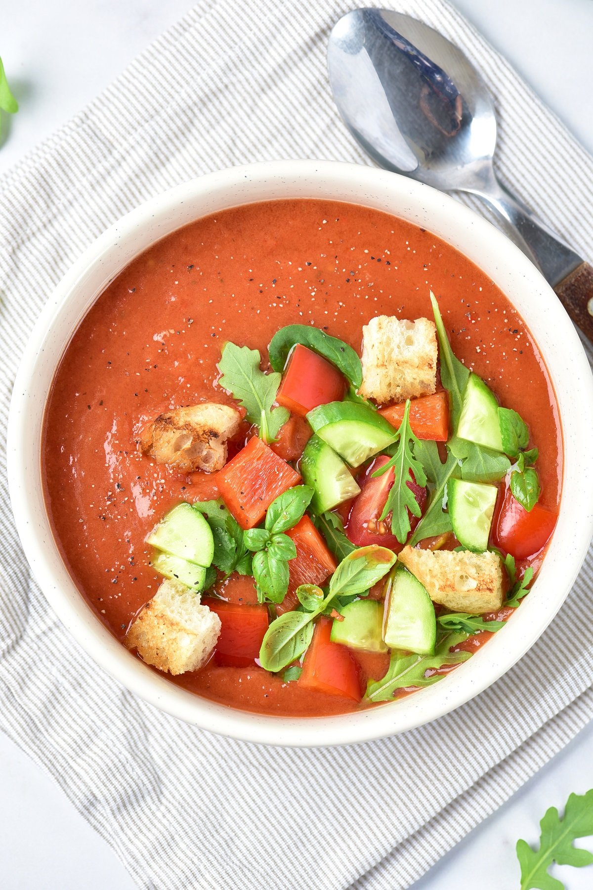 A bowl of fresh gazpacho topped with chopped veggies, croutons and basil.