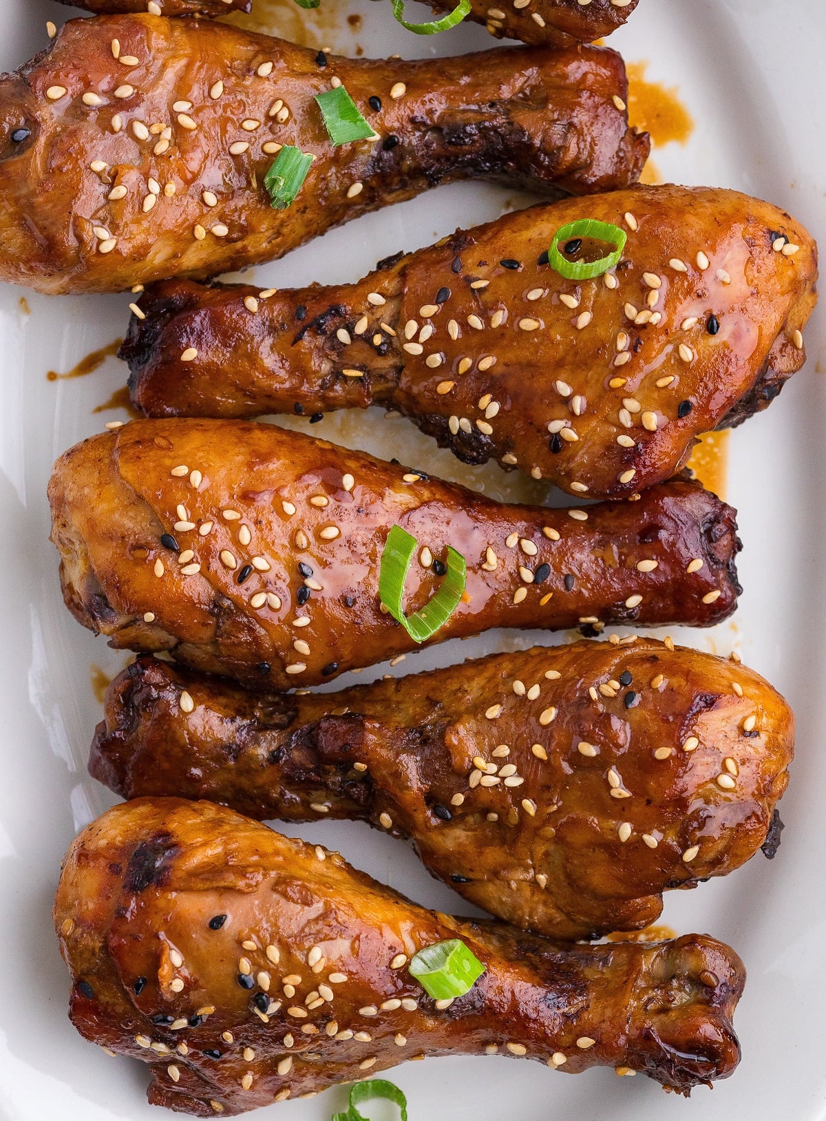 Teriyaki chicken legs garnished with sesame seeds and green onions on a platter. 