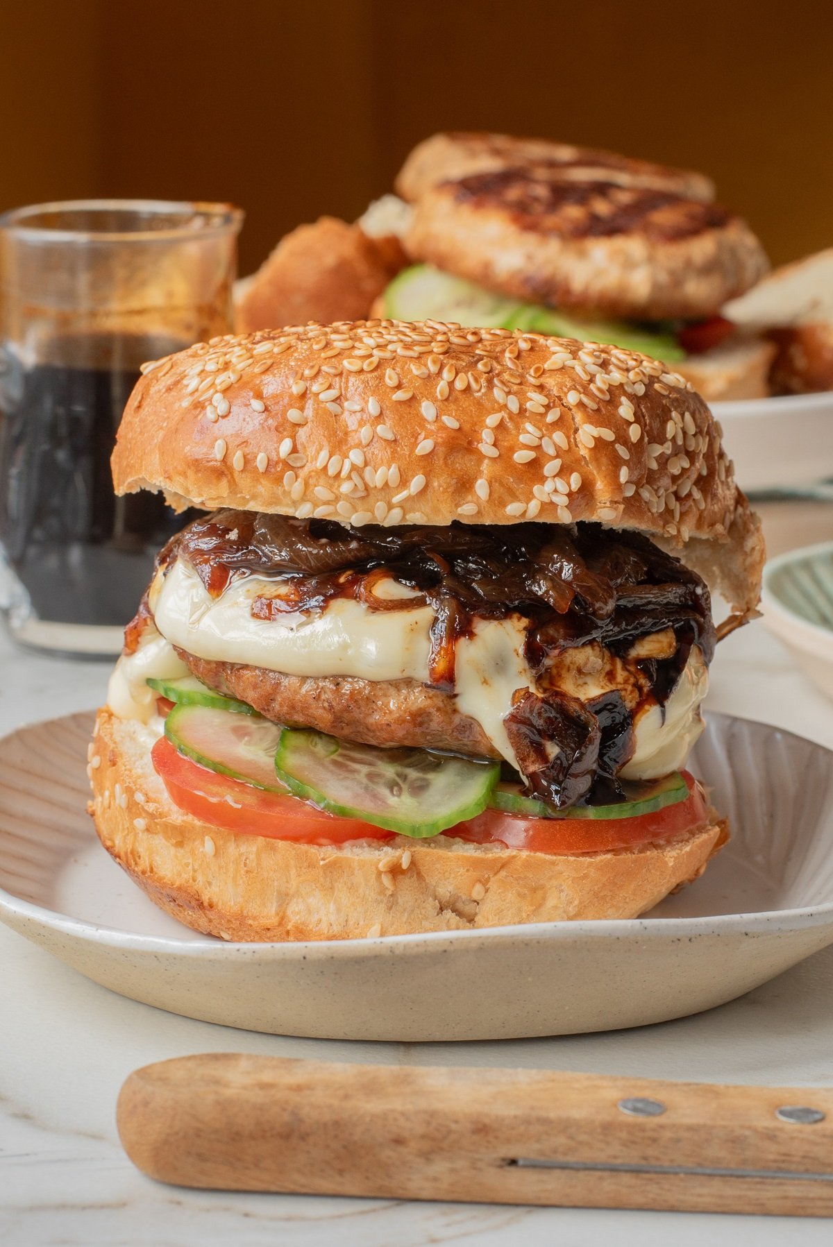 A chicken burger on a sesame seed bun topped with tomato, cucumber, onions and teriyaki sauce. 