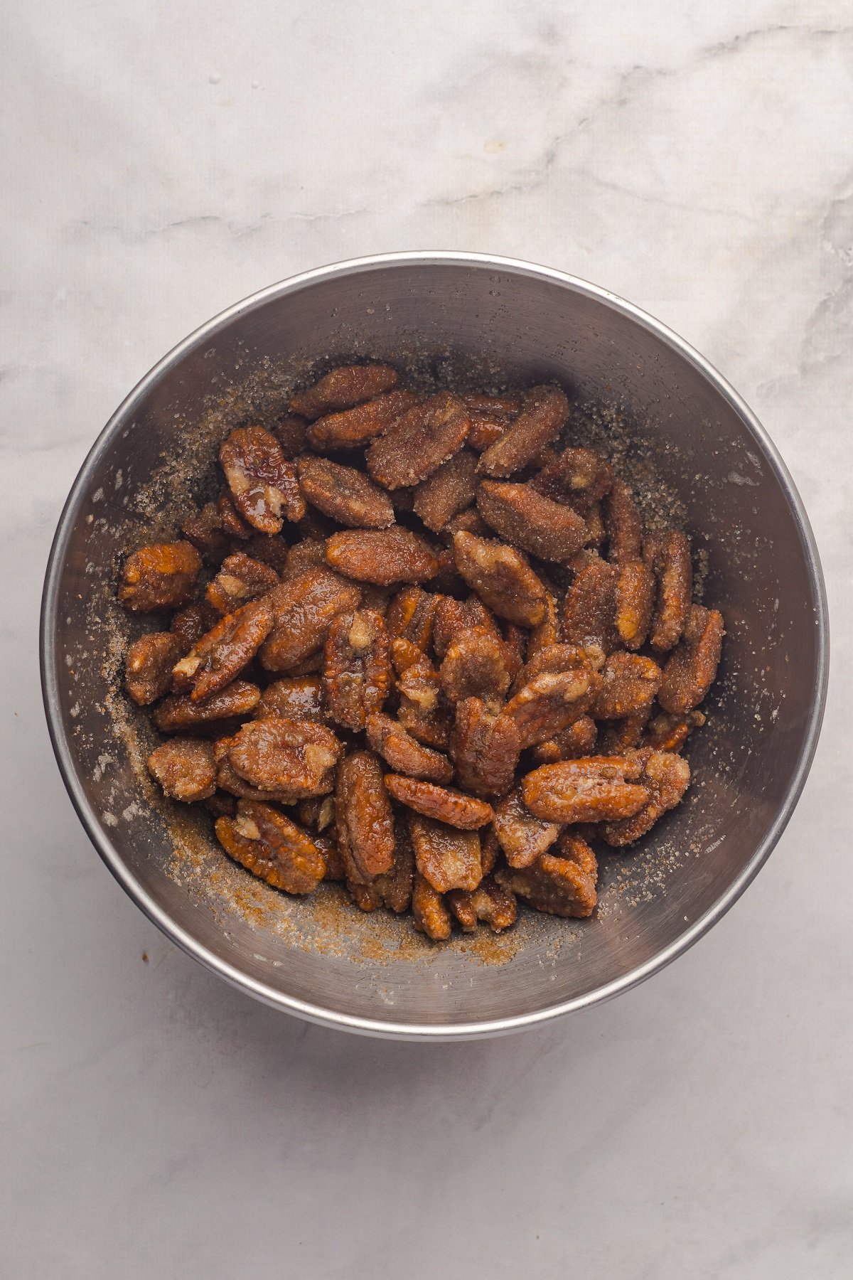Pecan halves are mixed with sugar and spices in a bowl.