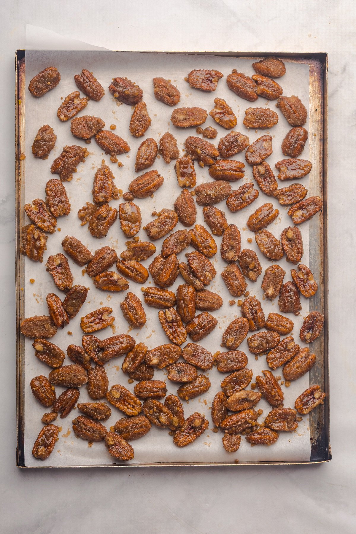 Pecans are spread on a large baking sheet lined with parchment.