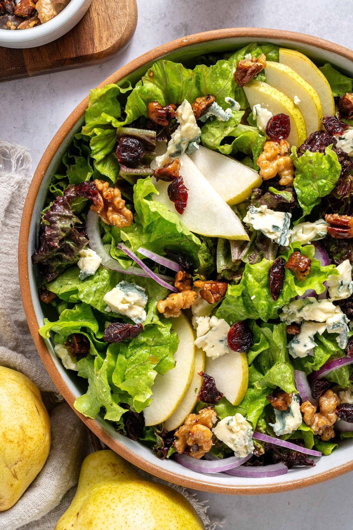 A large bowl with a salad topped with pears, gorgonzola cheese, nuts and cranberries. 