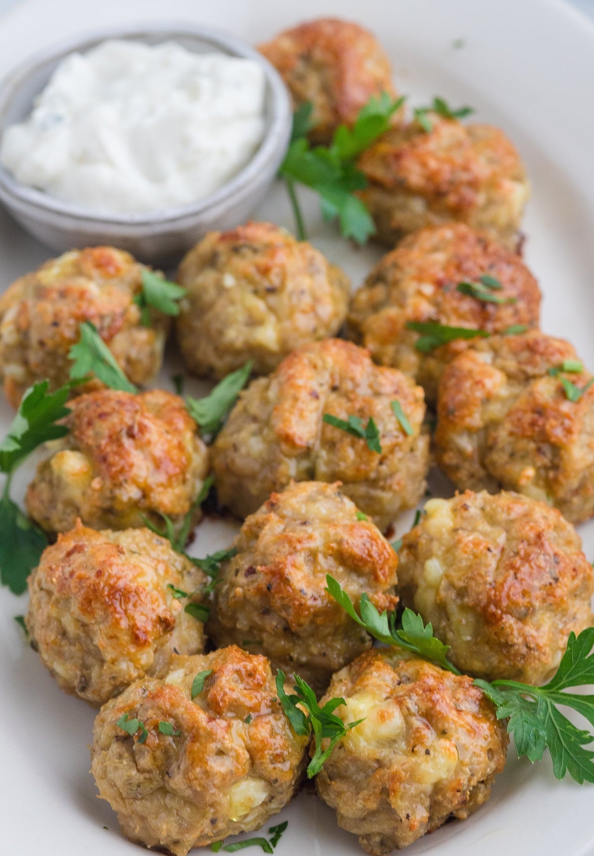 Greek chicken meatballs on a platter with dipping sauce. 