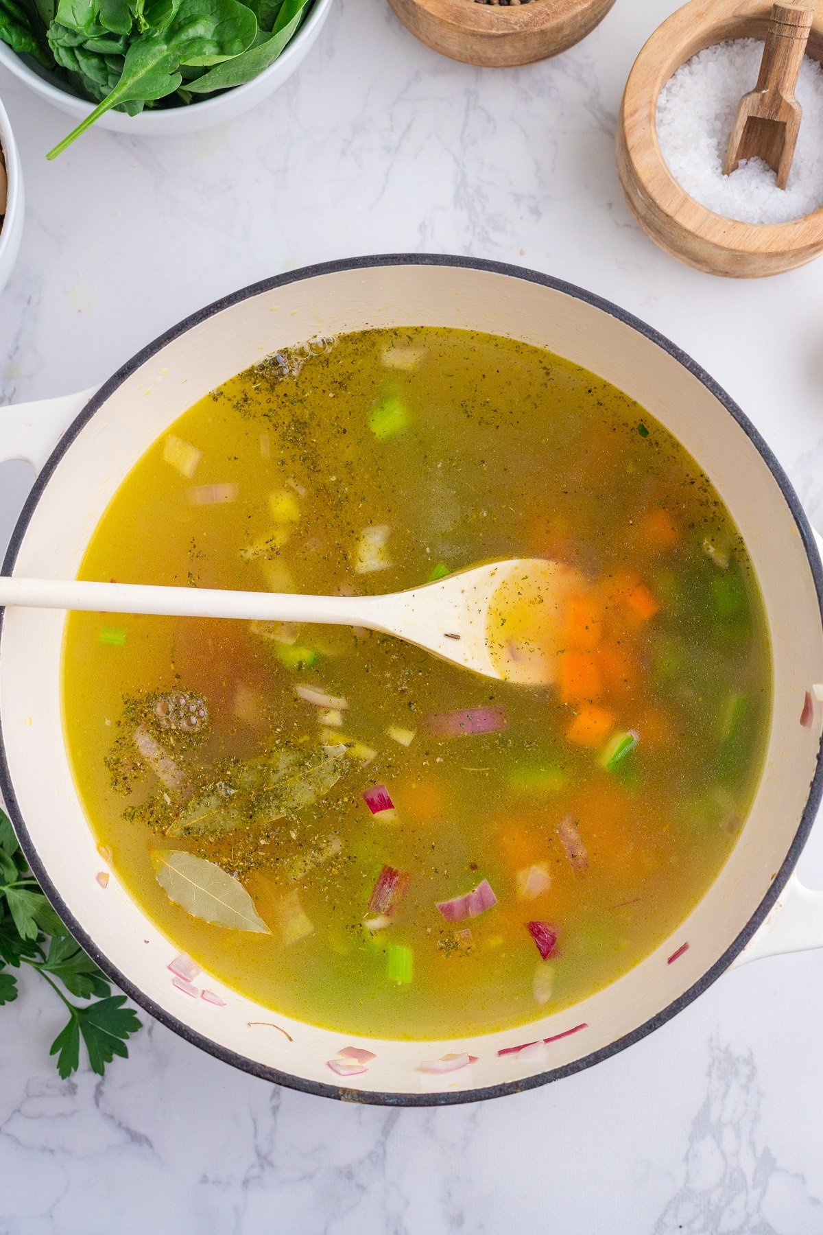 Broth is stirred in to the vegetables in a soup pot.