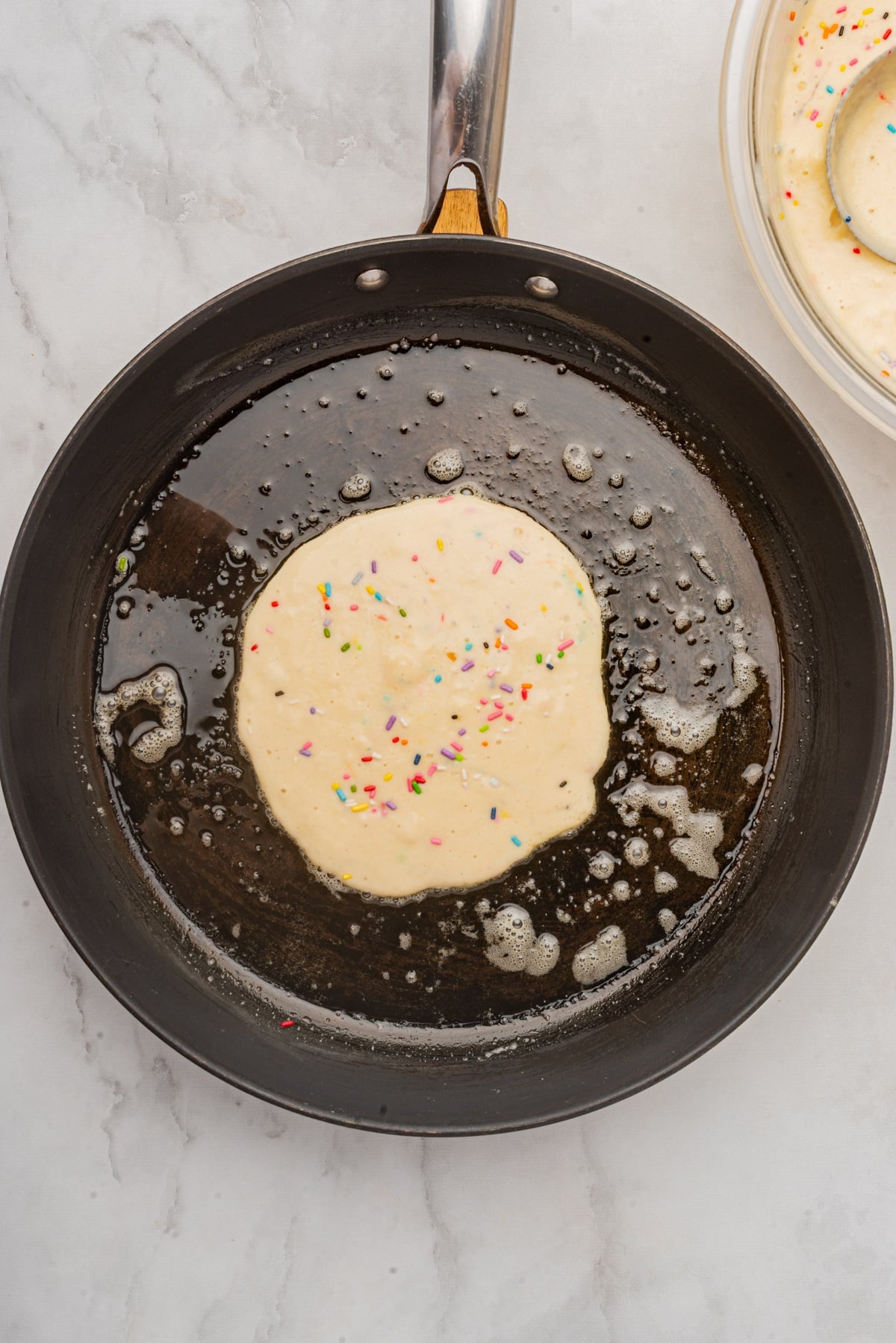 Pancake batter with sprinkles in a pan. 