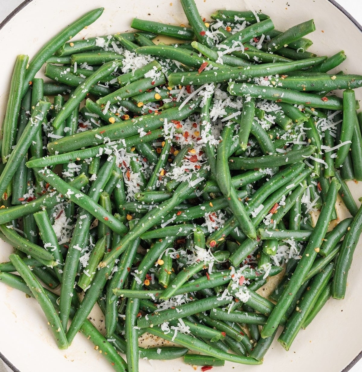 A plate of sauteed green beans topped with parmesan and red pepper flakes. 