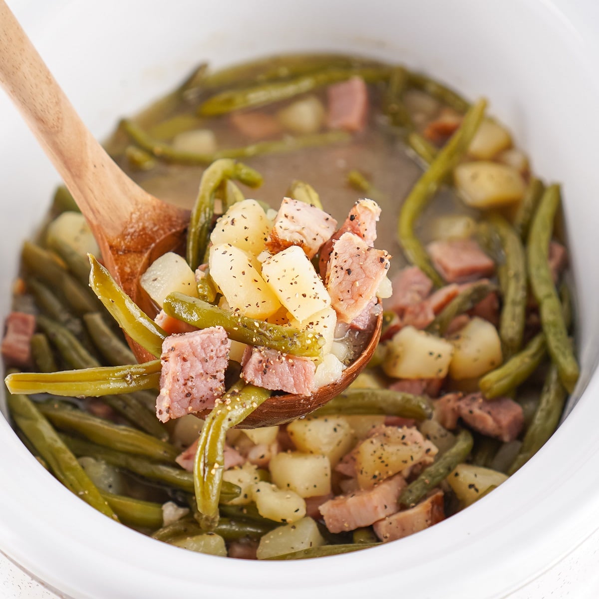 Green beans with potatoes and ham being spooned out of a crockpot.