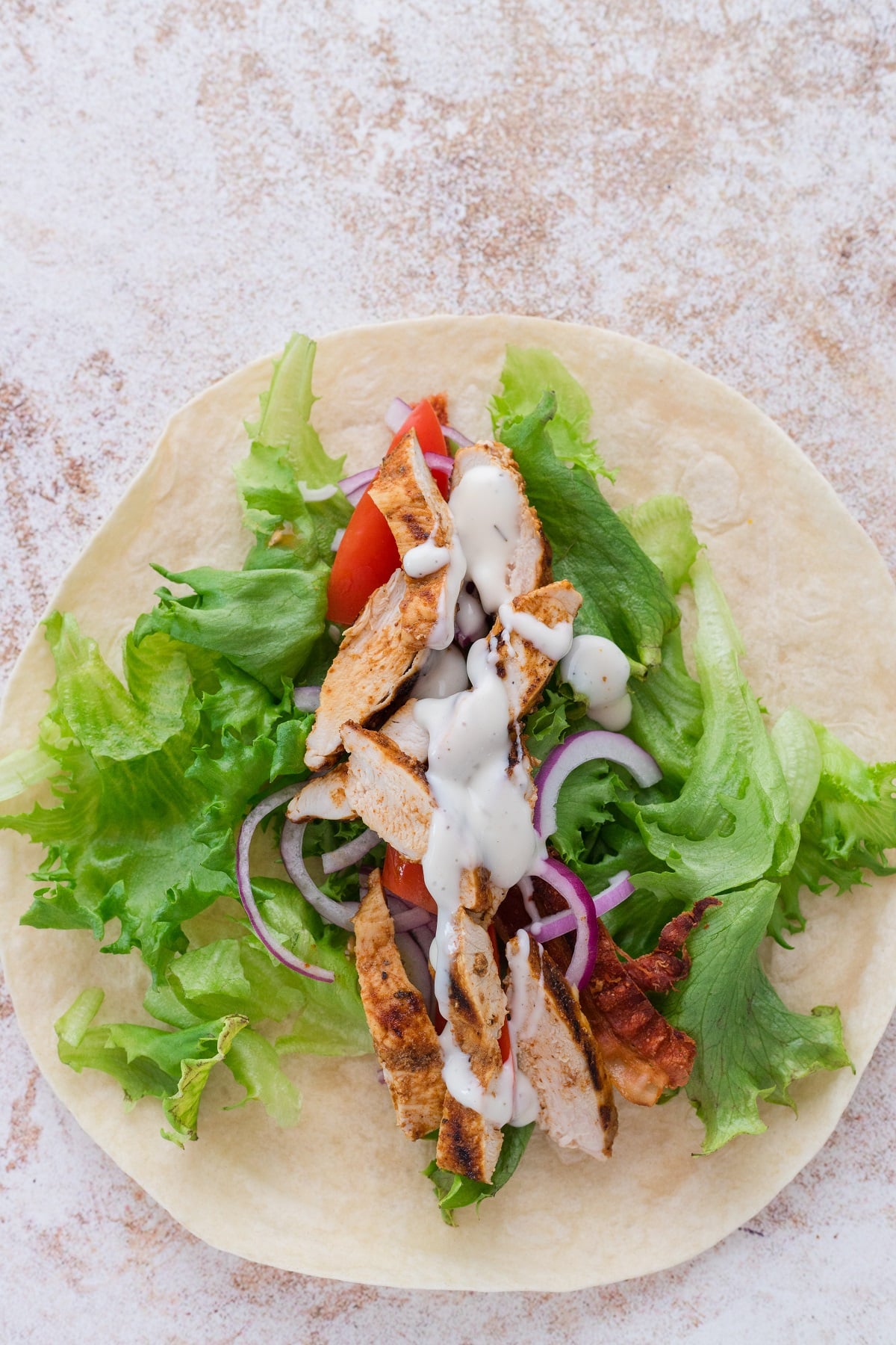 Grilled chicken wrap is assembled on a tortilla.
