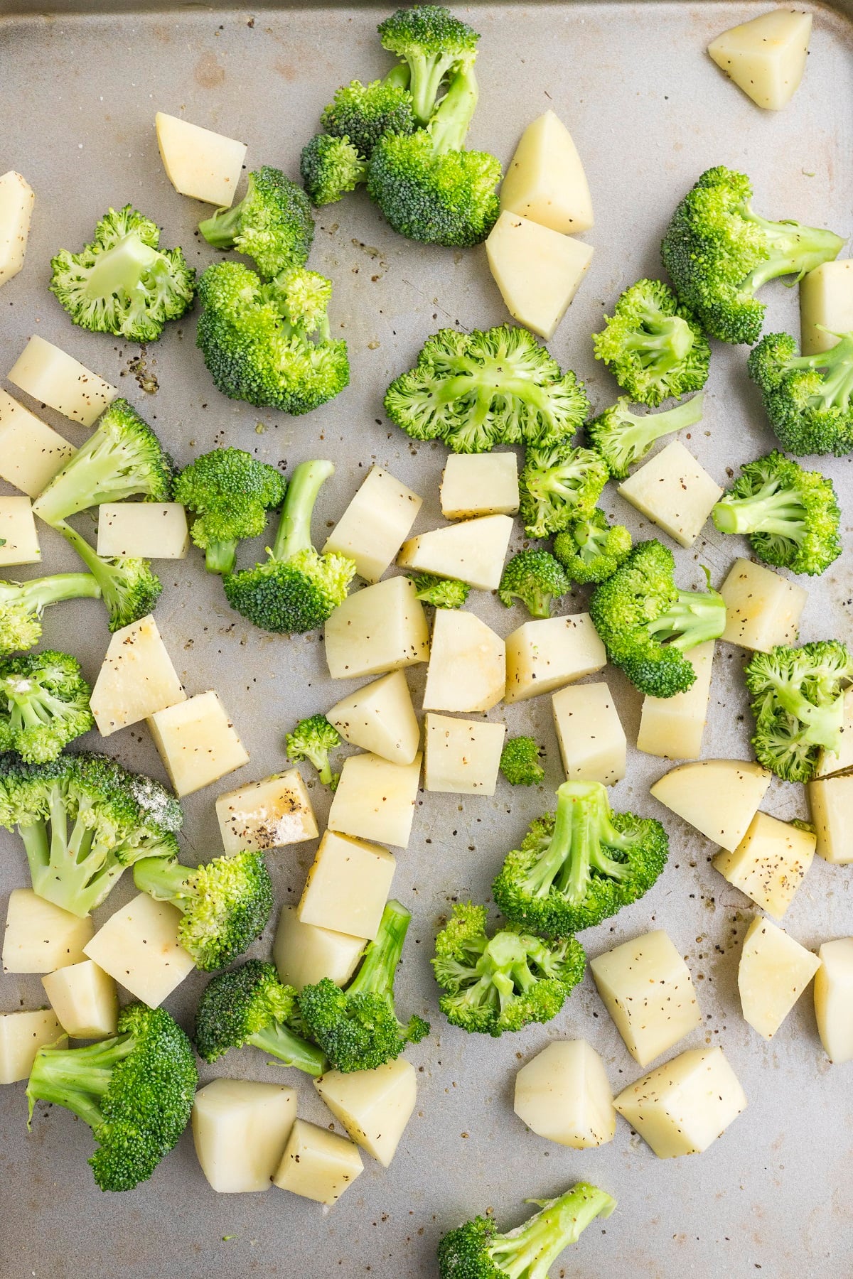 Cubbed potatoes and chopped broccoli are seasoned and arranged on a baking sheet.