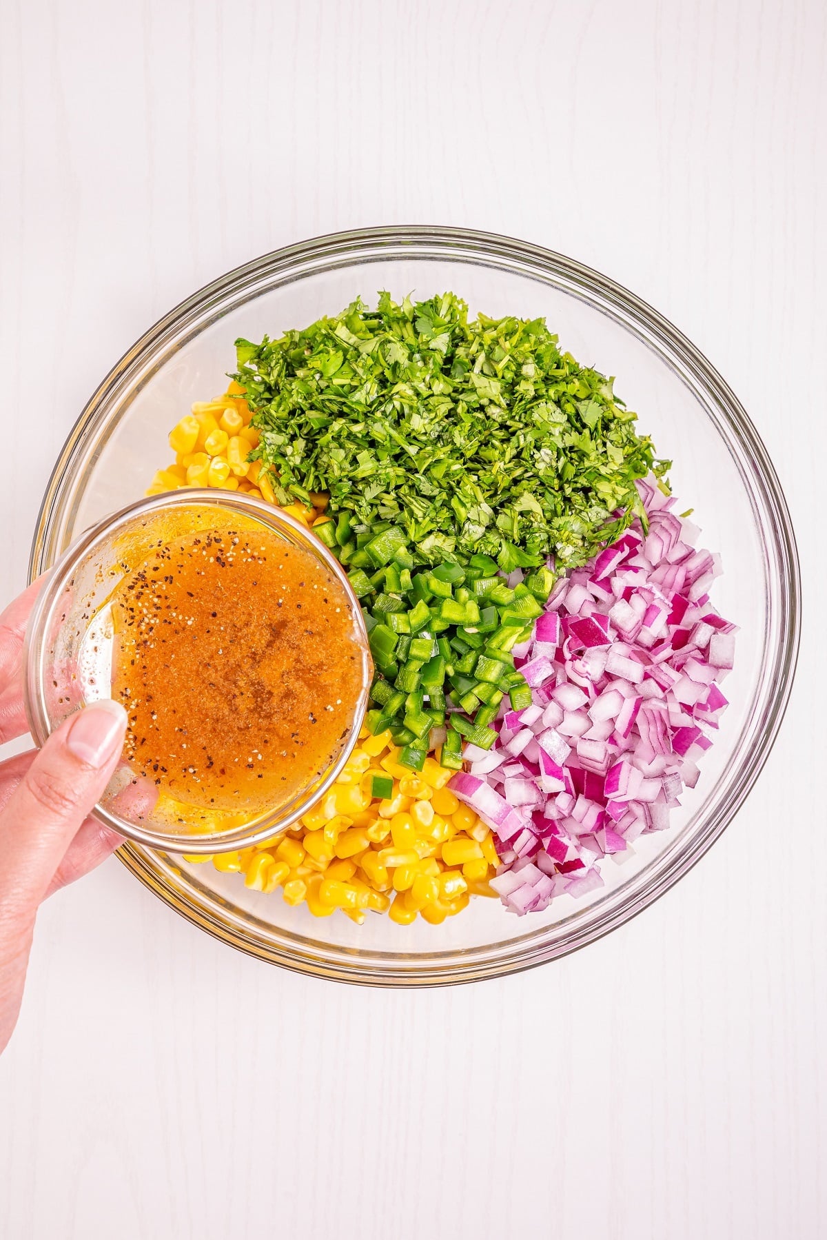 Corn salsa ingredients are combined in a bowl with the dressing. 