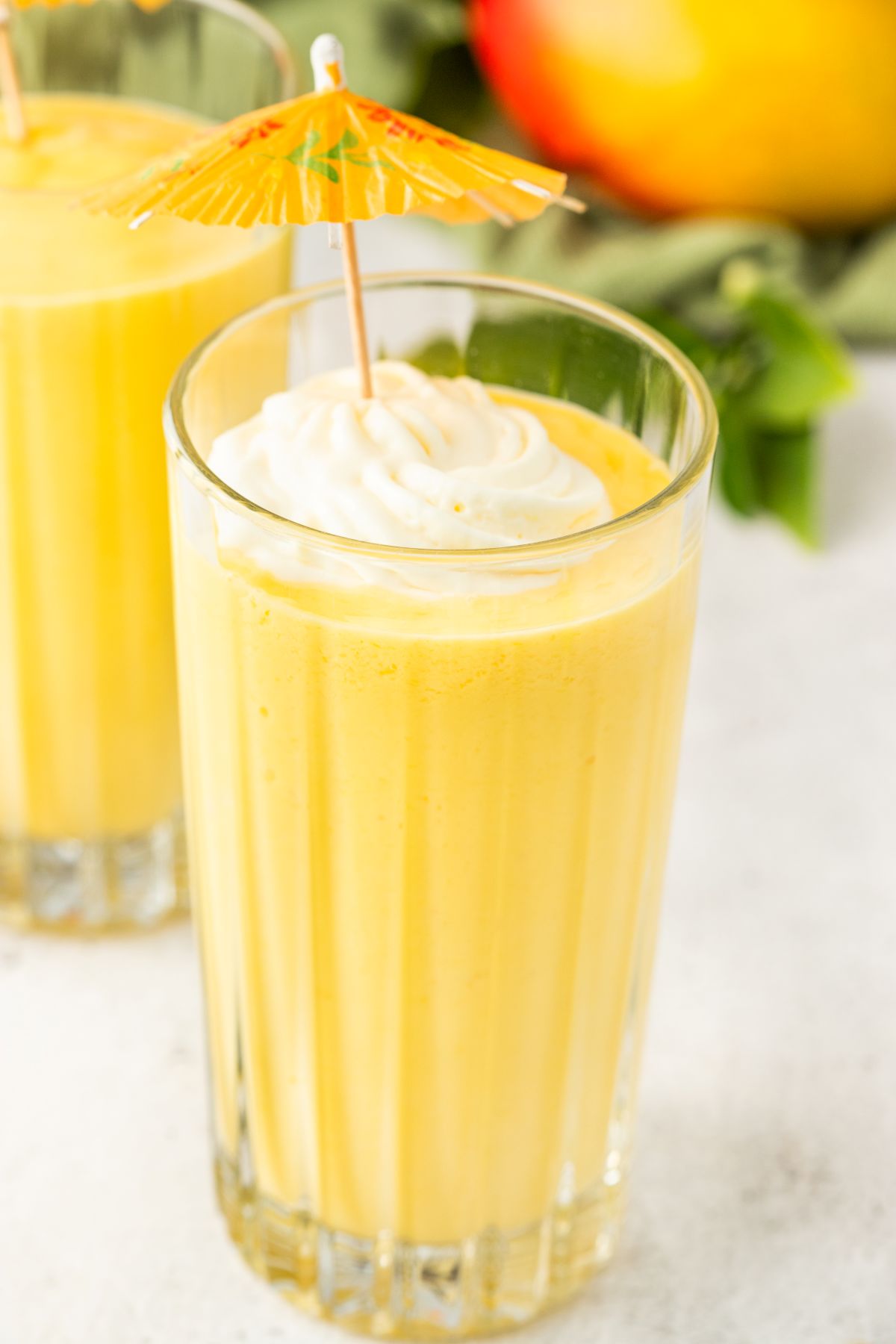 Mango shake recipe in a glass topped with whipped cream and a paper umbrella. 