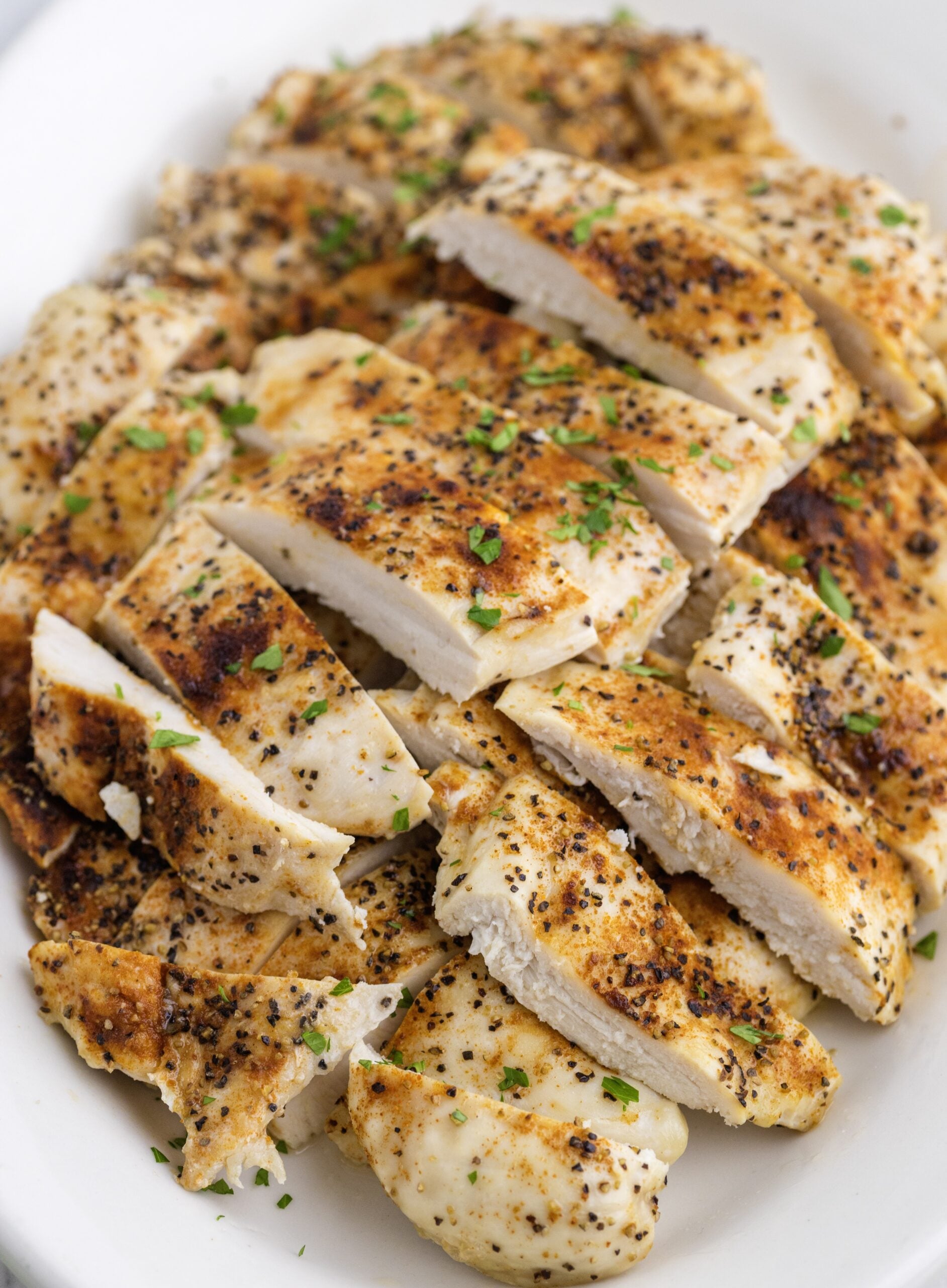 Seasoned, thin baked chicken breast sliced into pieces and piled on a platter.