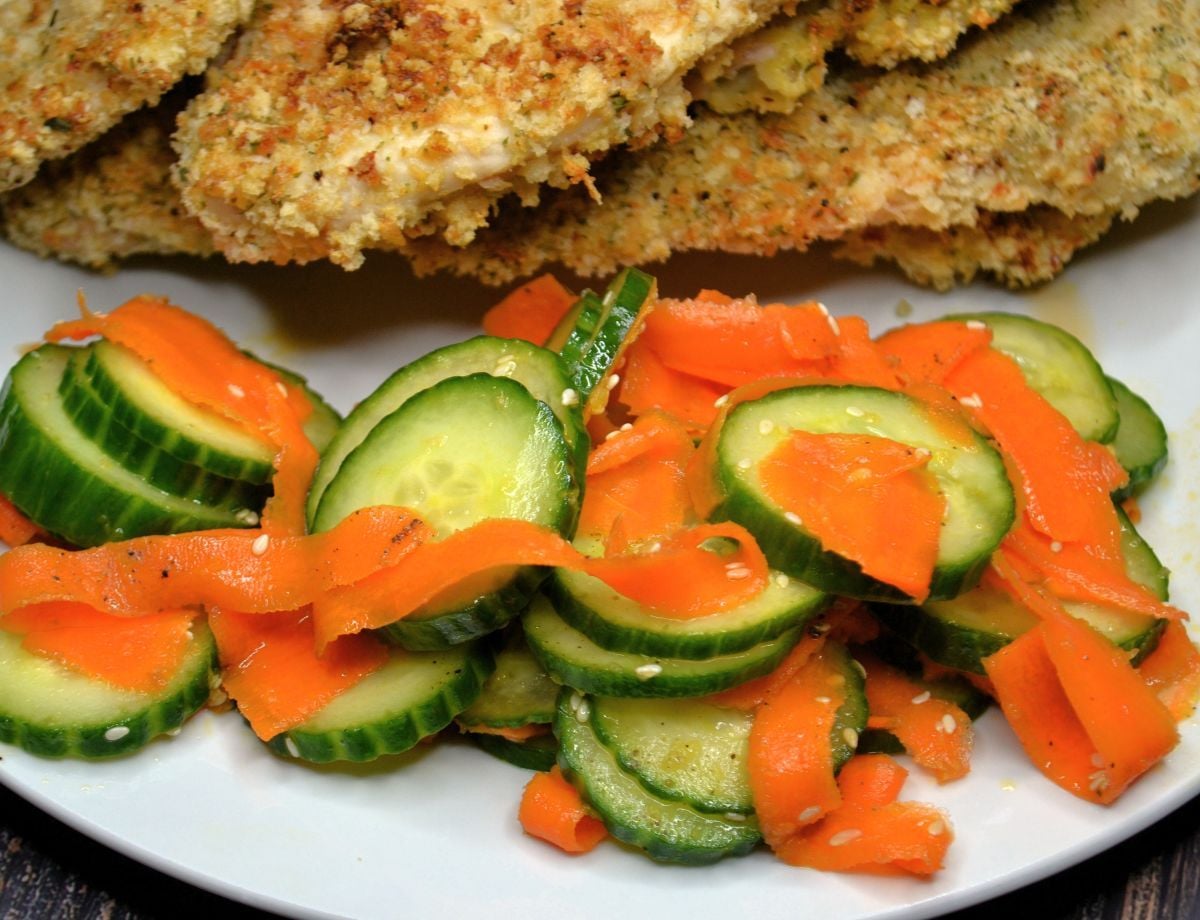 A plate of chicken with cucumber carrot salad on the side. 