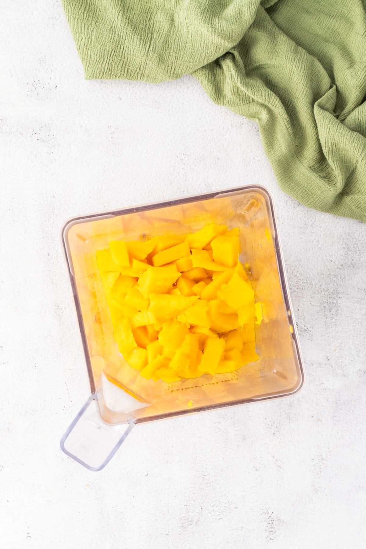 Fresh sliced mango is added to a blender. 