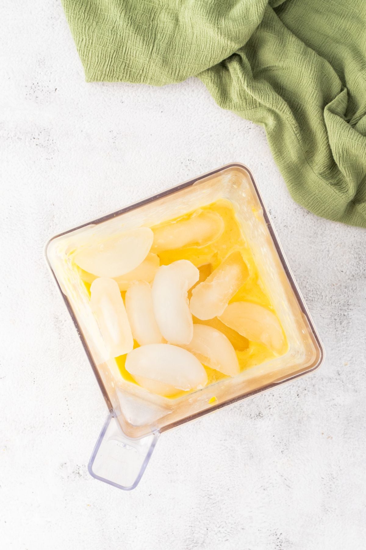 Ice is added to a blender with mango and milk. 