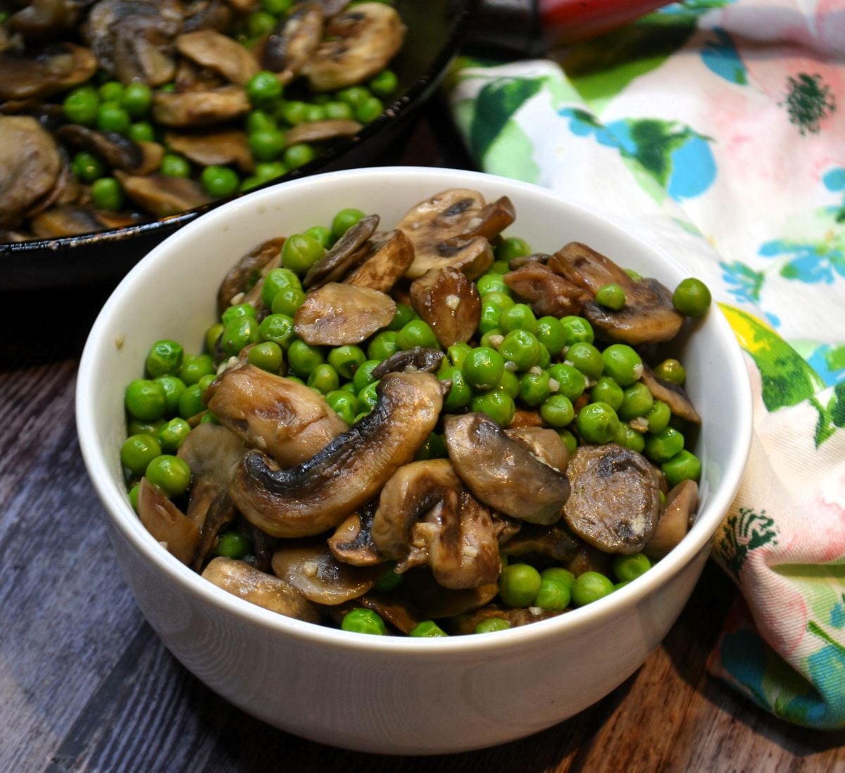 A white bowl with sauteed peas and mushrooms.