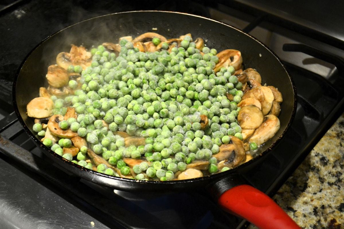 Frozen peas and sliced mushrooms in a skillet.