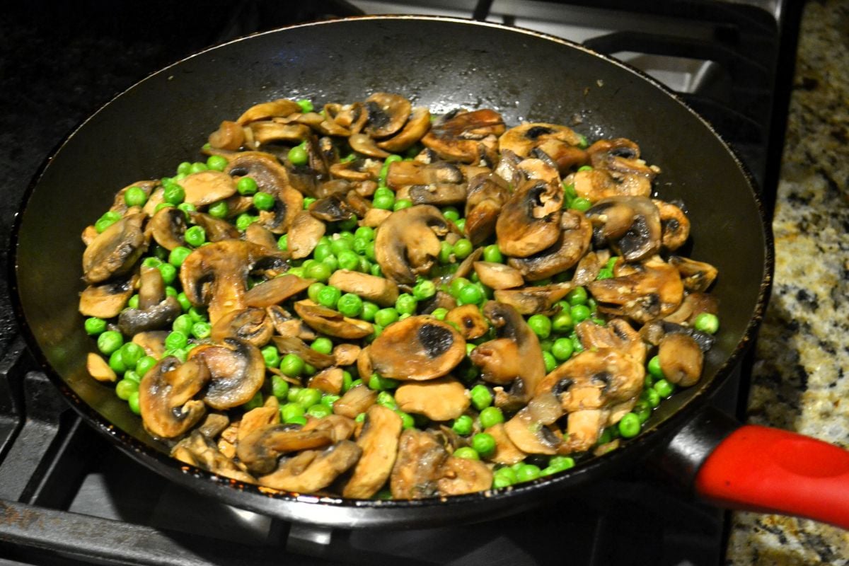 A skillet with sauteed peas and mushrooms.