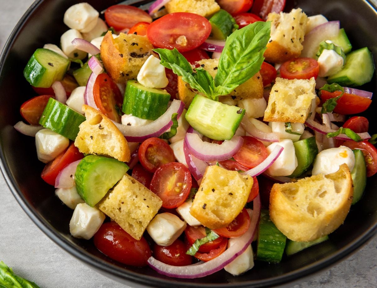 Panzanella salad garnished with basil in a black bowl.