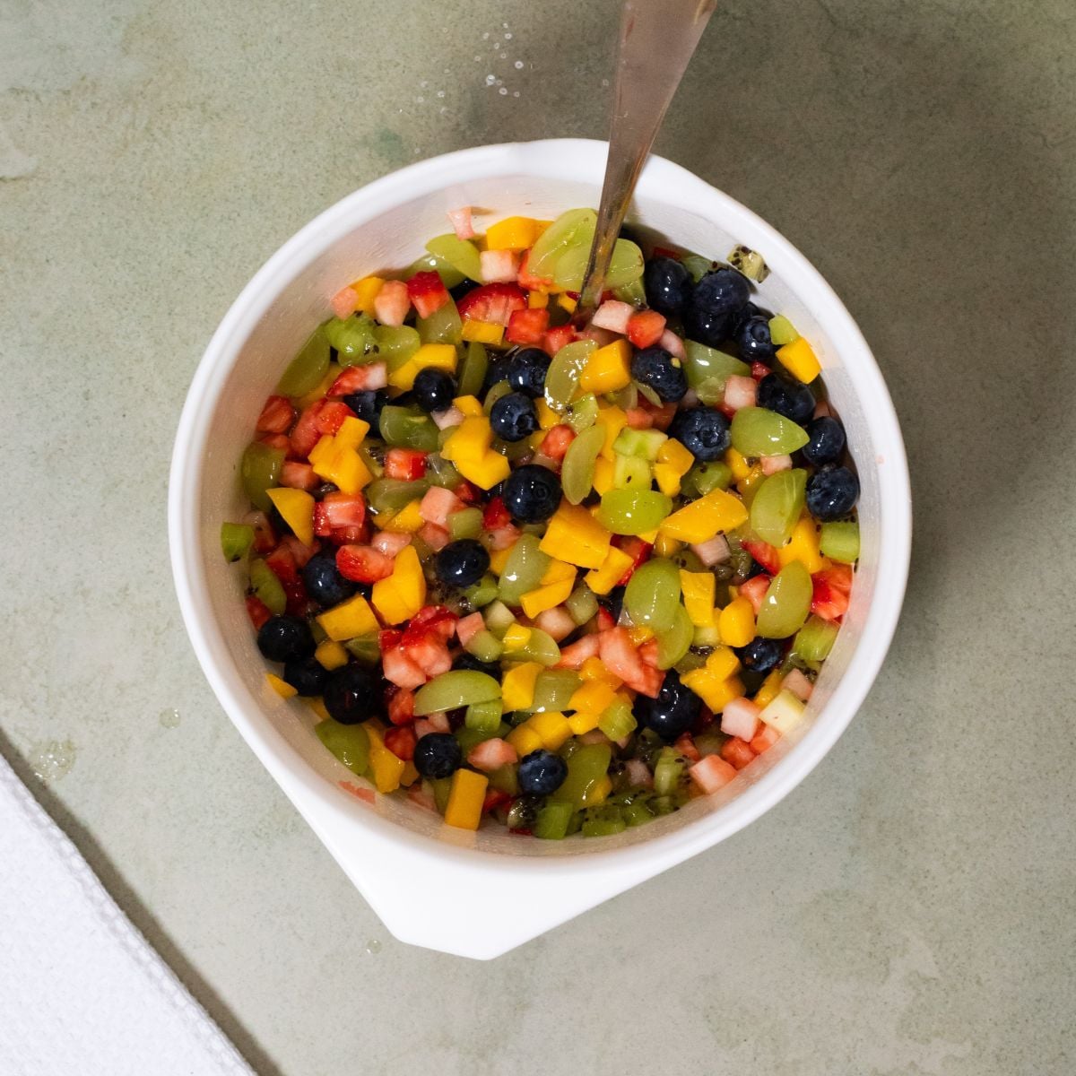 Sugar and lime juice is stirred with fruit in a bowl.