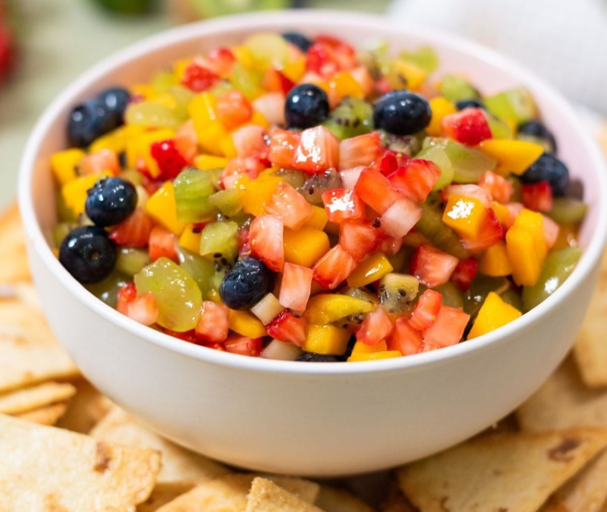 A bowl of fruit salsa surrounded by cinnamon sugar pita chips.