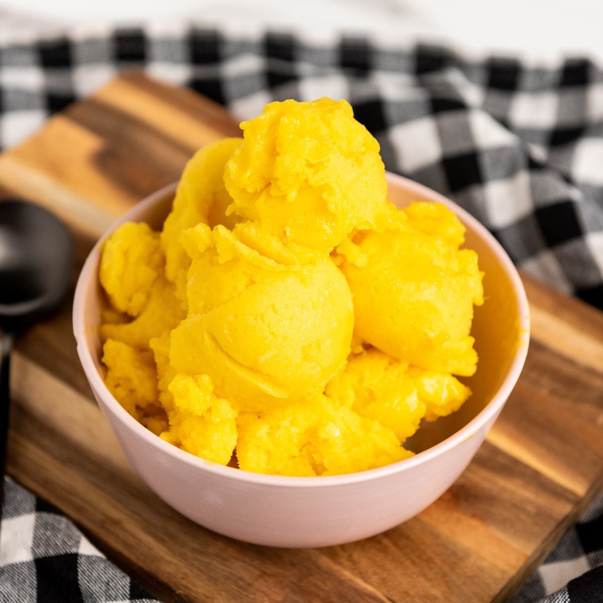 A big bowl of mango sorbet on a checkered cloth covered table.