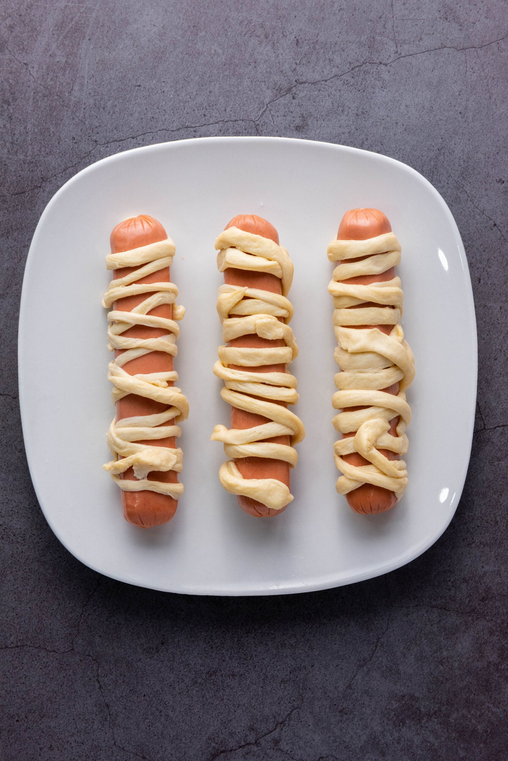 Crescent roll strips are wrapped around hot dogs.