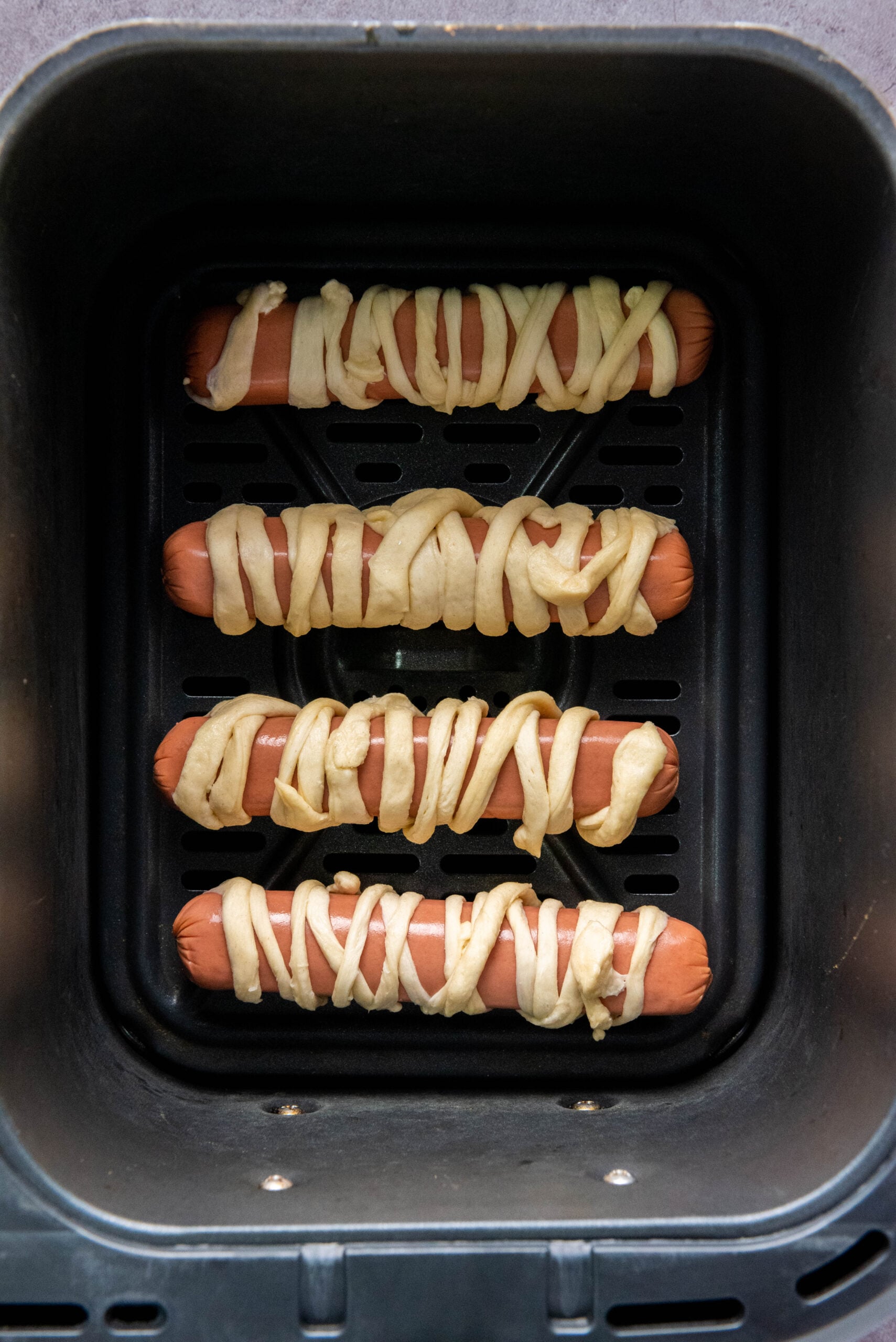 Crescent roll wrapped hot dogs are placed in the air fryer.